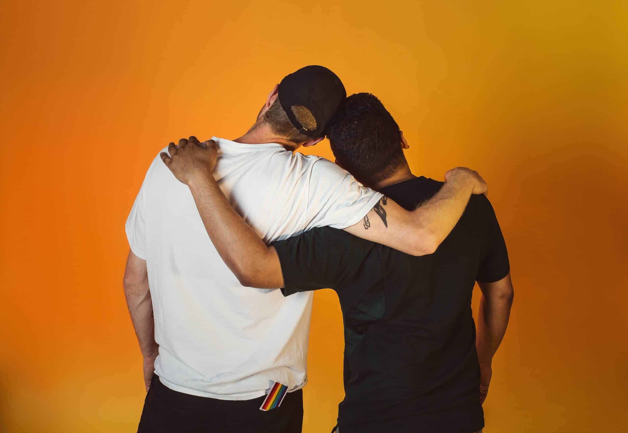 two men embrace each other against orange background