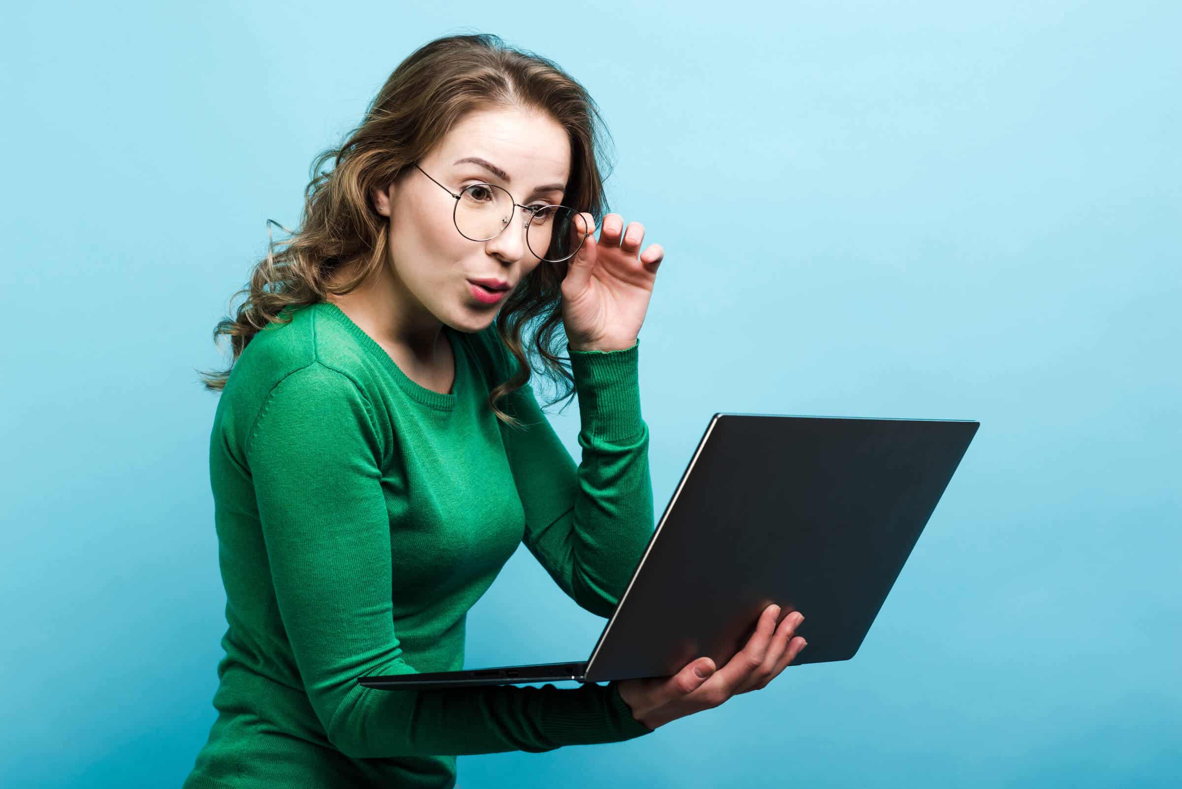girl in glasses surprised looking at laptop against a blue background