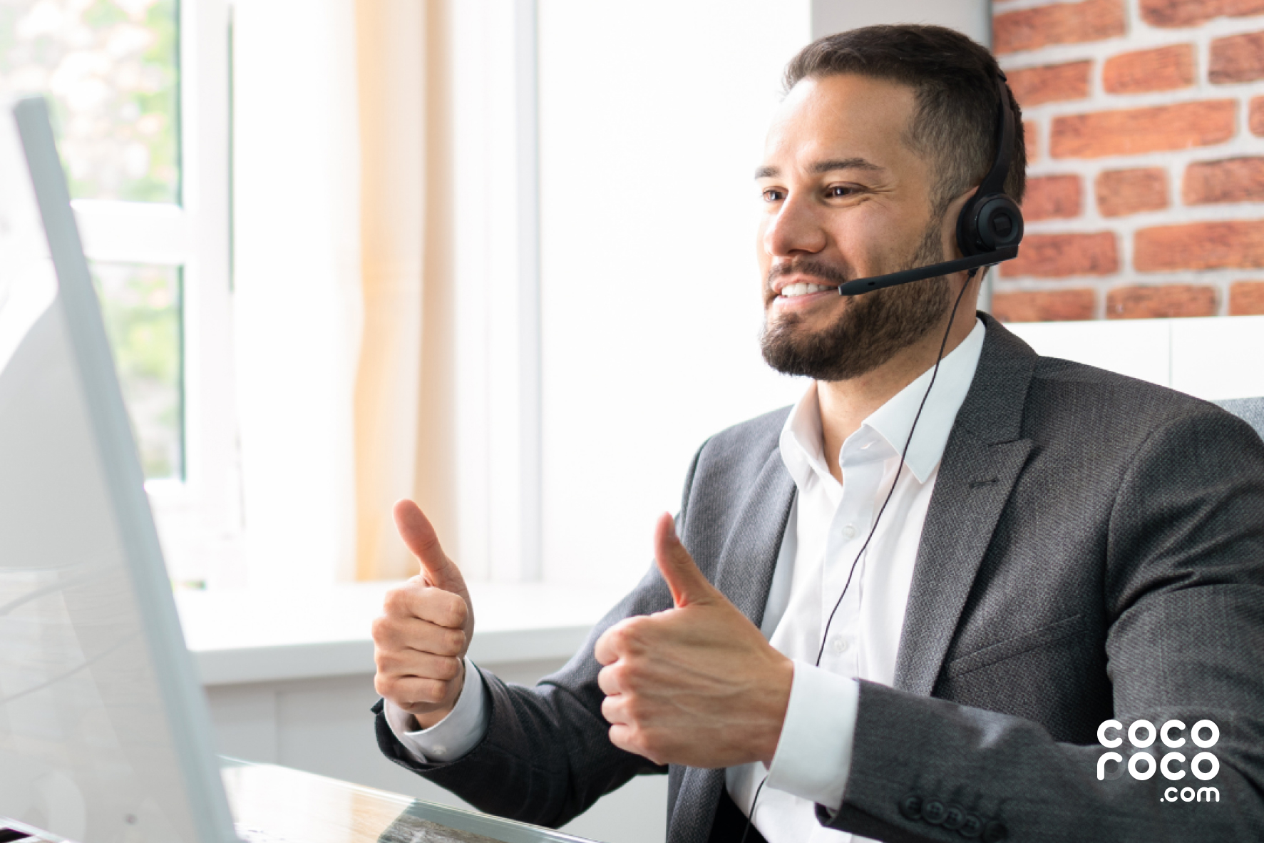 An image of a customer service agent smiling with both thumbs up. The agent is wearing a headset and appears to be helpful and approachable, conveying a positive attitude towards customers.